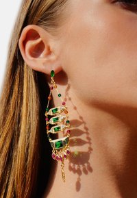 Boucles d'oreilles en or avec des gemstones verts et roses, design complexe avec plusieurs couches et accents décoratifs, projetant des ombres sur la peau.