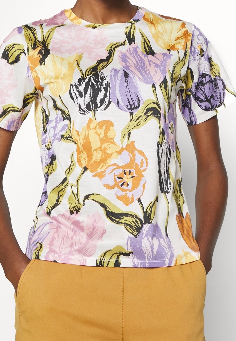 Camiseta de manga corta floral en blanco, con un estampado colorido de flores naranjas, rosas y moradas. Tejido suave con diseño de cuello redondo.