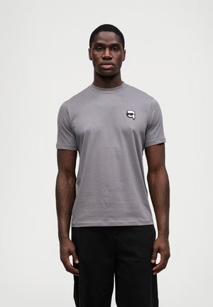 Pilkas trumpas rankovėmis marškinėliai, pagaminti iš medvilnės, su apykakle ir mažais grafikos akcentais kairiajame krūtinės srityje.