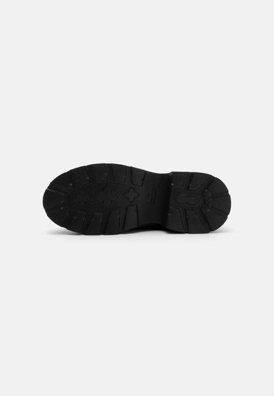 Suela de goma negra con una superficie texturizada, surcada con profundos surcos y un diseño en relieve, que ofrece tracción y estabilidad.