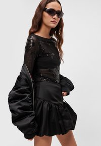 Fekete, áttetsző hosszú ujjú felső virágos flitteres díszítéssel, egy fekete szatén szoknyával, amely kampós szegéllyel rendelkezik, és egy fényes, párnázott dzseki.