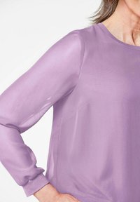 Lila Bluse mit langen, transparenten Ärmeln, Rundhalsausschnitt und glatter Textur. Verfügt über subtile Nähdetails und eine lockere Passform.