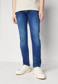 Blå denimjeans med smal passform, med en klassisk femficksdesign och kontrasterande sömmar, i kombination med vita sneakers.