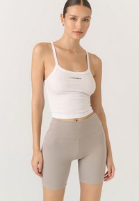 Biały prążkowany crop top z logo "LAMANIA", w połączeniu z beżowymi szortami o wysokim stanie. Obie odzieże są dopasowane i gładkie w dotyku.
