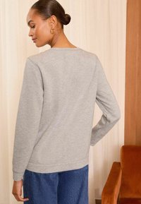 Felpa grigia a maniche lunghe con una vestibilità comoda e polsini a coste, abbinata a pantaloni blu a gamba larga. Tensione del tessuto semplice e liscia.