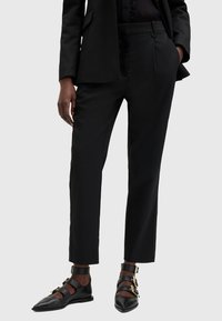 Svarta skräddarsydda byxor i mjukt tyg med smal passform och sidofickor. Kombineras med svarta läderskor med gulddetaljer.