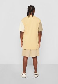 T-shirt à manches courtes, bicolore beige et crème, assorti à un short beige. Le tissu semble doux avec une coupe décontractée.