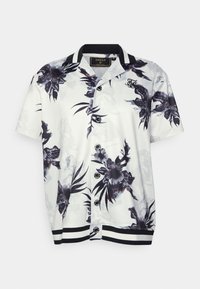 Camisa blanca de manga corta con botones, estampado floral en negro y gris, cuello y dobladillo a rayas, y logo bordado en el pecho.