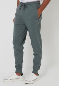 Graue Baumwoll-Jogginghosen mit einem elastischen Bund, Kordelzug, Seitentaschen und gerippten Bündchen. Kombiniert mit weißen Sneakers.