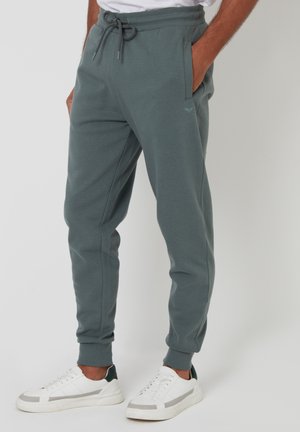 Graue Baumwoll-Jogginghosen mit einem elastischen Bund, Kordelzug, Seitentaschen und gerippten Bündchen. Kombiniert mit weißen Sneakers.