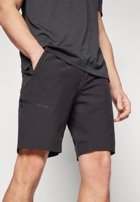 Svarta shorts i ett lättviktigt material, med en sidficka med dragkedja och rak skärning, med fållen som når mitt på låret.