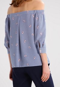 Modrá a bílá pruhovaná blůza bez ramínek s růžovými květinovými vzory, elastickým výstřihem a ohrnutými tříčtvrtečními rukávy. Hladká textura.