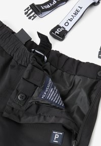 Zwarte outdoor broek met elastische tailleband, binnenzak met label en verstelbare banden. Materiaal lijkt duurzaam en waterafstotend.
