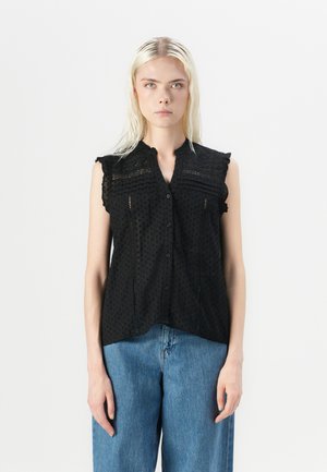 Svart ermela bluse med prikkemønster, volangdetaljer på skuldrene og knappeåpning. Stoffet har en teksturert og lett utseende.