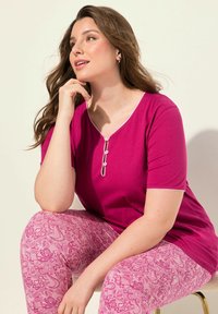 Magenta korte mouwen top met een v-hals en decoratieve knoopdetails, gecombineerd met roze leggings met een patroon met bloemmotieven.