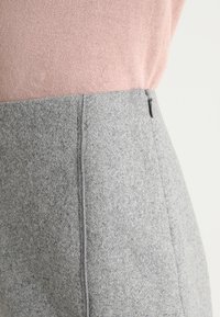 Grå filt kjol med en slät textur, med en sidodragkedja och rena linjer. Kombinerad med en ljusrosa stickad topp.