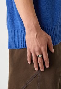 Blue textured sweater with ribbed hem, paired with brown fabric pants, displaying a hand wearing a silver ring with an oval detail.