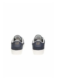 Sneakers blu navy con un pannello posteriore in suede e suola in gomma bianca. Presentano il logo "GAP" in oro sul tallone. Design bicolore, stile minimalista.