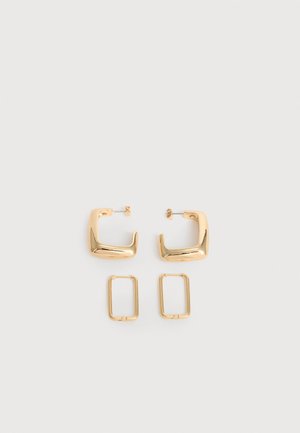 Deux paires de Boucles d'oreilles créoles géométriques dorées sur une surface blanche unie, une paire carrée et pleine, une paire rectangulaire et creuse.