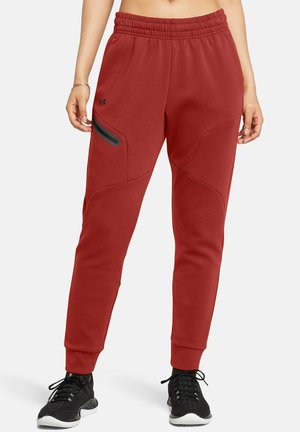 Pantaloni da tuta rossi con cintura elastica, tasche laterali e dettagli neri. Texture liscia e vestibilità affusolata. Abbinati a scarpe da ginnastica nere.