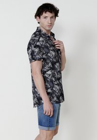 Camisa negra de manga corta con patrones de hojas blancas, cuello abotonado; combinada con pantalones cortos de mezclilla enrollados. Tejido suave, corte relajado.