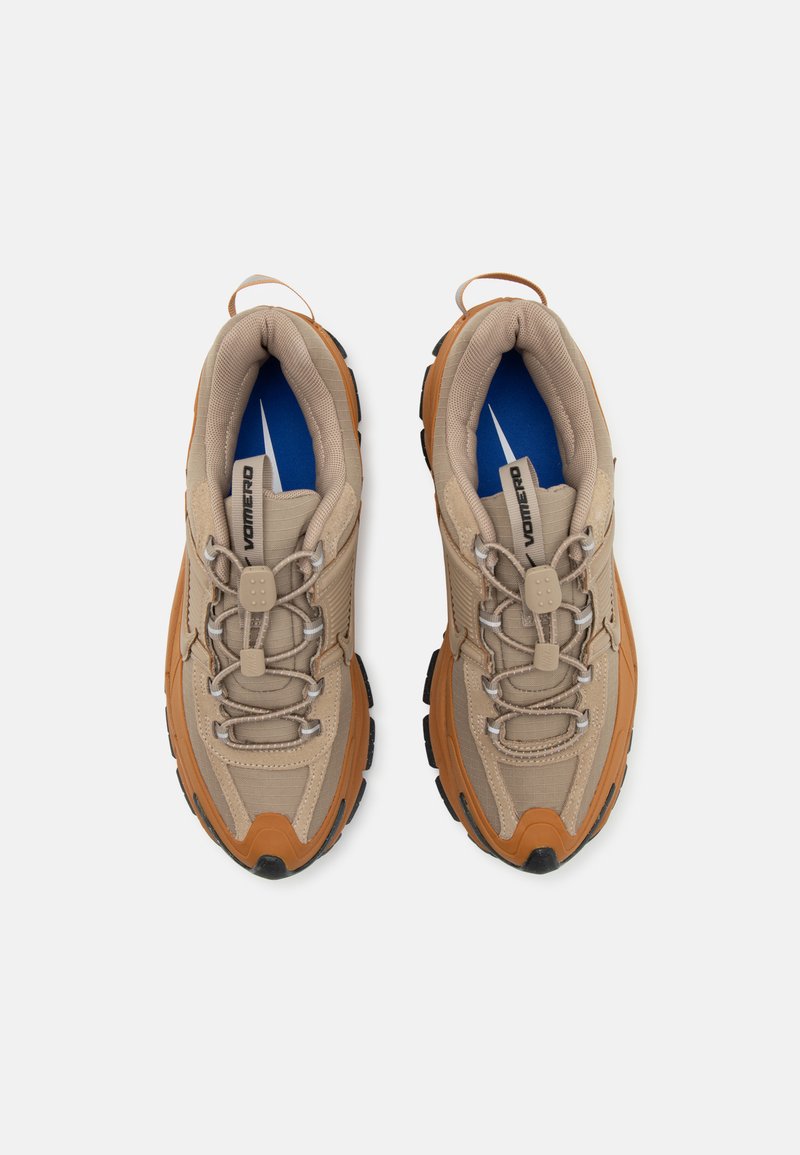 Beige sportieve schoenen met een gestructureerde bovenkant, oranje accenten, grijze veters en een blauwe binnenzool. Dikke rubberen buitenzool voor grip.