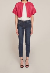 Röd läderkort jacka med volangärmar, kombinerad med en vit topp och mörk denim skinny jeans. Svarta klackar med remmar fulländar looken.