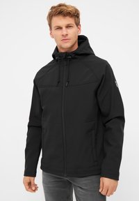 Giacca softshell nera con cappuccio, zip frontale e cordini regolabili. Texture liscia, dotata di tasche laterali e di una discreta patch con logo.