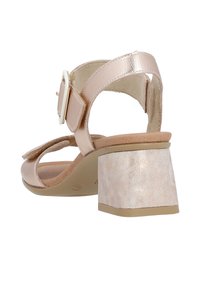 Sandalia de tacón en oro rosa con acabado metálico, tira ajustable en el tobillo y un tacón cuadrado de superficie texturizada.