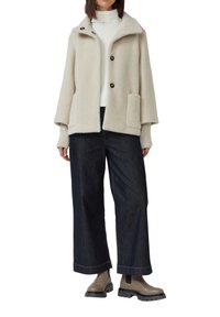 Beige wollen blend jasje met grote kraag, twee knopen en zak. Gecombineerd met een donker denim broek met wijde pijpen en beige enkellaarsjes.