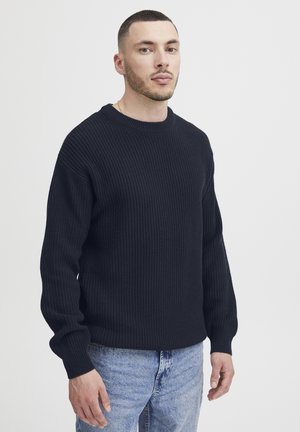 Dark navy ribbed sweater with a crew neckline and long sleeves, paired with light blue denim. Features a textured knit pattern.
