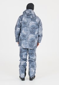 Lumilautailutakki ja housut siniharmaassa marmoroidussa kuosissa. Takissa on huppu ja se on löysä malli. Housut ovat myös löysät ja niissä on säädettävät lahkeet.