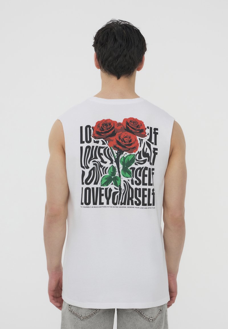 Maglietta bianca senza maniche con una grafica di rose rosse e testo nero che riporta frasi come "AMATI" sul retro.