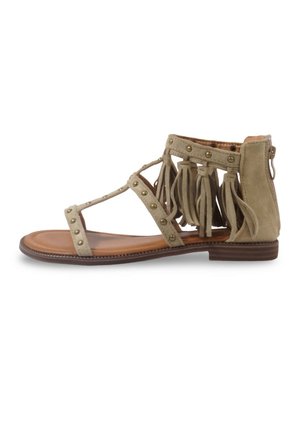 Sandale plate beige avec brides cloutées, détails en franges autour de la cheville, fermeture éclair à l'arrière et semelle marron.
