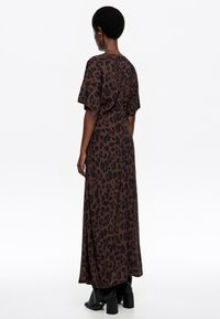 Maxikleid mit braunem Leopardenmuster, kurzen, weiten Ärmeln, lockerer Passform und glatter Textur, kombiniert mit schwarzen, Blockabsatz-Stiefeln.