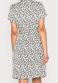 Blommönstrad klänning i svart med vita och gula blommor, korta ärmar, åtsittande midja och utsvängd kjol. Lättviktsmaterial med subtil textur.