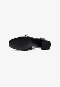 Scarpa in pelle nera con tacco a blocco, caratterizzata da una texture liscia, una cinghia con dettagli in fibbia e una suola in gomma con motivo per una migliore aderenza.