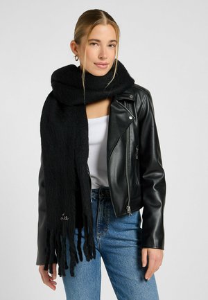 Schwarzer Wollgemischschal mit fransigen Kanten, getragen über einem weißen Oberteil und einer schwarzen Lederjacke. Glatte Textur, leichtes Design.