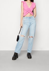 Růžový top s krátkým rukávem, s volánovými okraji a nařasením, zkombinovaný se světle modrými roztrhanými džíny a černými platformovými botami.