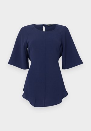 Blouse bleu marine pour femme avec encolure ronde, manches courtes évasées, fermeture à bouton avec ouverture en forme de goutte dans le dos, et ourlet légèrement arrondi.