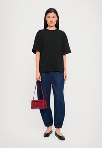 Μαύρο oversized μπλουζάκι με κοντά μανίκια, συνδυασμένο με φαρδιά μπλε τζιν παντελόνια. Συμπληρωμένο με μια μικρή κόκκινη τσάντα και μαύρες μπαλαρίνες.