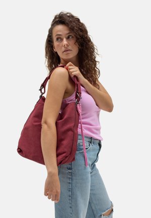 Rote Stoffschultertasche mit weicher Textur, geschwungenem Design und einem abnehmbaren pinken Kordelakzent. Verfügt über Metallbeschläge und kontrastierende Nähte.