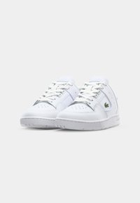 Białe buty sportowe z gładkiej skórzanej cholewki, perforowanym noskiem, białymi sznurowadłami i małym zielonym logo z boku. Płaska gumowa podeszwa.