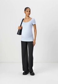Top azul-claro de manga curta, calças largas pretas e mala de ombro preta. Tecido suave com um design ajustado que acentua uma barriga redonda.
