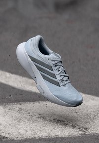 Ανοιχτό γαλάζιο αθλητικό παπούτσι τρεξίματος με υφασμάτινη επιφάνεια, τρεις γκρι ρίγες και λευκή σόλα, με στρογγυλή μύτη και σχεδιασμό με κορδόνια.