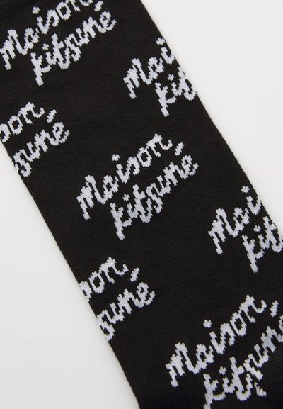Black socks featuring a repeating white text pattern that spells "Maison Kitsuné" in a cursive font. Smooth knit texture.