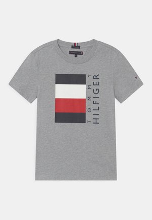 Szara bawełniana koszulka z krótkim rękawem z logo flagi Tommy Hilfiger w kolorach czarnym, białym i czerwonym oraz pionowym napisem "Tommy Hilfiger" na przodzie.