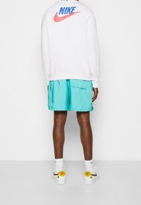 Vit sweatshirt med blå och röd Nike-logotyp, kombinerad med turkosa shorts och vita sneakers med gula detaljer.