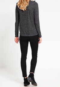 Grauer Langarmoberteil mit einer glatten Textur und subtilen Nähdetails, kombiniert mit schwarzen Slim-Fit-Hosen und schwarzen Stiefeletten.