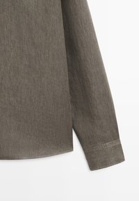 Brauner Ärmelaufschlag eines Langarmshirts mit sichtbaren Saumdetails auf weißem Hintergrund, zeigt einen Teil des Ärmels und Saum.